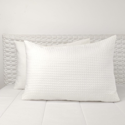 Almofadas brancas texturizadas em cama com cabeceira acamada branca