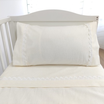 Almofada branca bordada numa cama branca com cabeceira de madeira