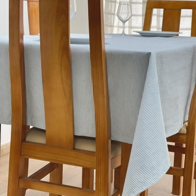 Mesa de jantar em madeira clara com toalha azul listrada e cadeiras de madeira