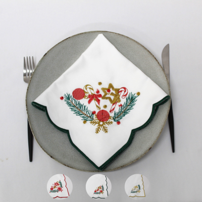Guardanapo branco bordado com motivos natalícios num prato cinza com talheres