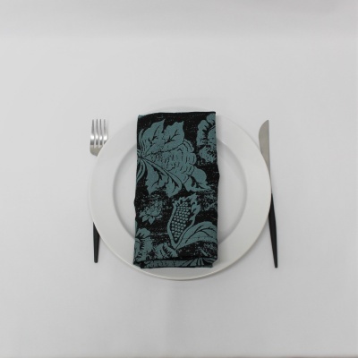 Guardanapo decorativo verde escuro e preto sobre prato branco com talheres à mesa