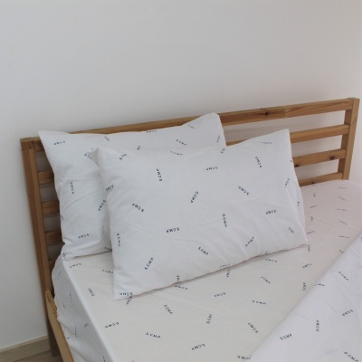 Conjunto de roupa de cama branco com letras pretas sobre cama de madeira clara