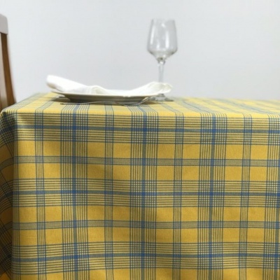 Mesa com toalha amarelo xadrez, prato branco, guardanapo branco e copo de vinho de vidro