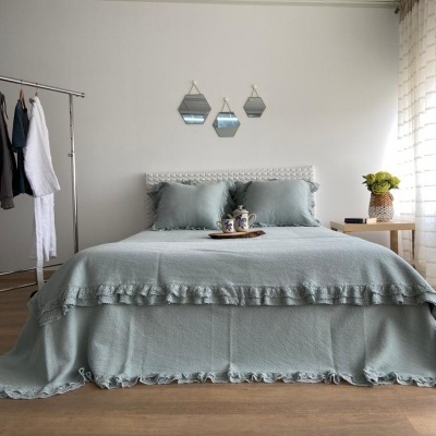 Cama com roupa de cama verde-água e decoração minimalista, incluindo espelhos hexagonais e mesa com flores.