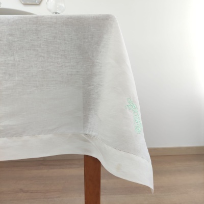 Toalha de mesa branca com bordado verde claro numa sala com chão de madeira clara