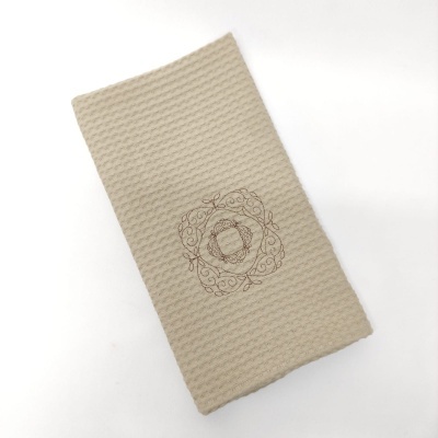 Toalha de mão bege com bordado castanho e textura tipo waffle