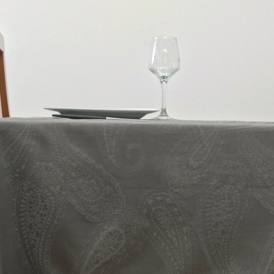 Toalha de mesa cinzenta com padrão, copo de vidro e pratos brancos numa mesa com cadeira de madeira