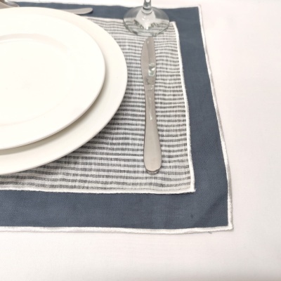 Jogo americano listrado cinza e azul colocado em mesa com pratos brancos e talheres