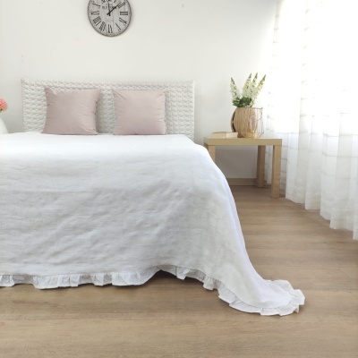 quarto com cama branca, almofadas rosas, relógio de parede e mesa com vaso e flores