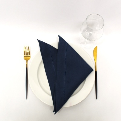 Mesa posta com prato branco, guardanapo azul, talheres preto e dourado e copo transparente