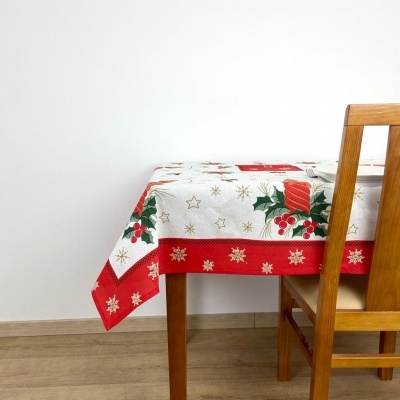 Toalha de mesa natalícia com padrões vermelhos, verdes e dourados sobre mesa de madeira com cadeira.