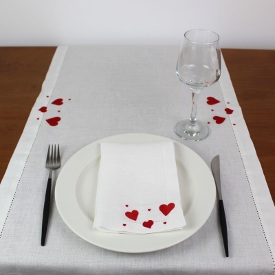 Toalha de mesa branca com corações vermelhos, prato branco, talheres pretos e copo de vidro