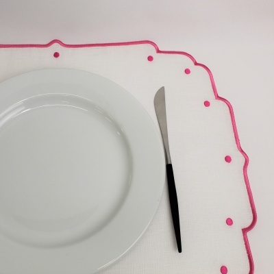 Lugar de mesa com prato branco, faca preta e toalha branca com bordas e pontos rosa.