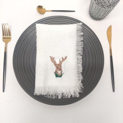 Mesa posta com prato cinza, guardanapo branco bordado com veado, talheres pretos e dourados e copo transparente