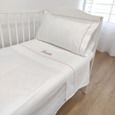 Jogo de cama branco com linha rosa e bordado vermelho, numa cama branca de madeira, com janela e cortina ao fundo
