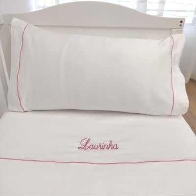 Jogo de cama branco com bordas e bordados rosas num berço