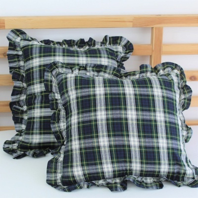 Duas almofadas xadrez com bordas franzidas sobre cama de madeira clara