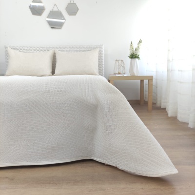 Colcha branca com padrão geométrico em relevo e almofadas na cama em quarto claro com móveis de madeira