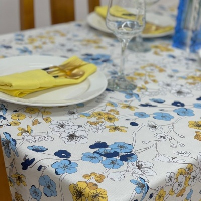Toalha de mesa floral em azul e amarelo com pratos brancos e guardanapos amarelos numa mesa