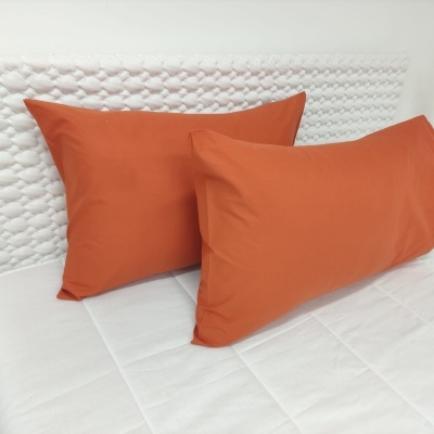 Duas almofadas laranja sobre edredão branco com cabeceira branca texturizada