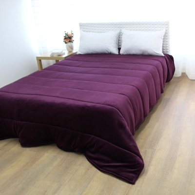 Colcha roxa de veludo numa cama branca com duas almofadas brancas