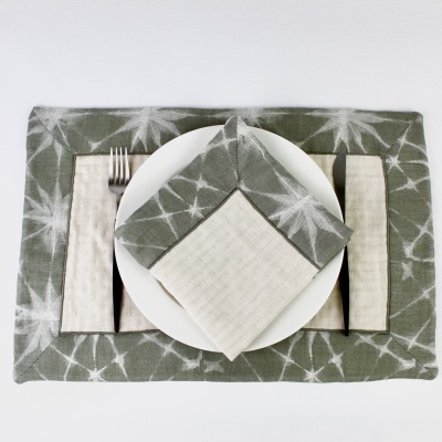 Conjunto de guardanapos e pega para talheres cinza e branco sobre prato branco com talheres.