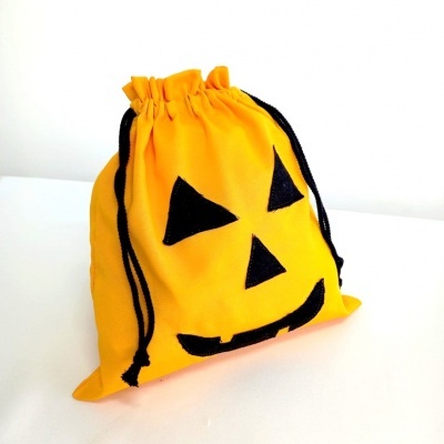Saco amarelo de tecido com rosto de abóbora preto e cordões pretos