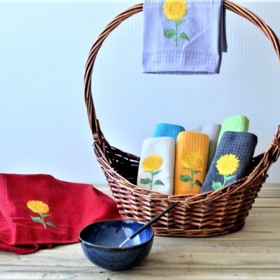 Cesto de vime com toalhas coloridas bordadas com girassol sobre mesa de madeira clara