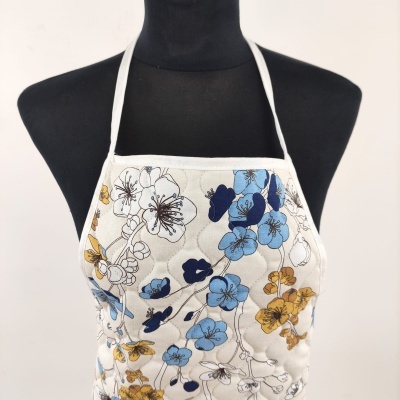 Avental branco com padrão floral azul e amarelo em manequim preto