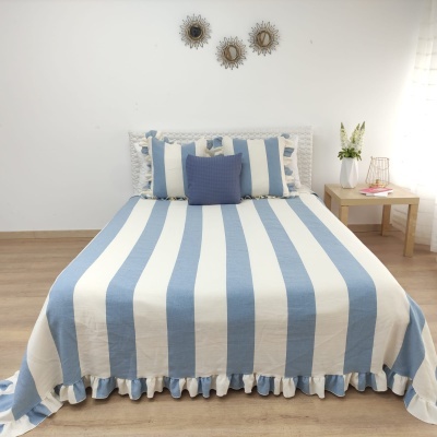 Cama com colcha azul e branca riscada e folho, com almofadas e cabeceira branca rendada.