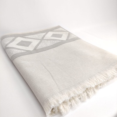 Manta branca com padrão cinzento claro de losangos e franjas nas extremidades