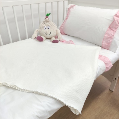 Cama de criança branca com roupa de cama branca e rosa, manta branca e boneco de pelúcia algodão com face sorridente