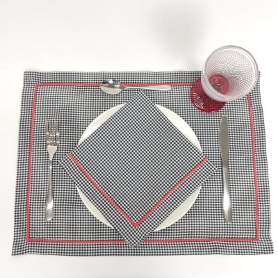 Jogo americano xadrez preto e branco com bordas vermelhas em mesa com louça e talheres