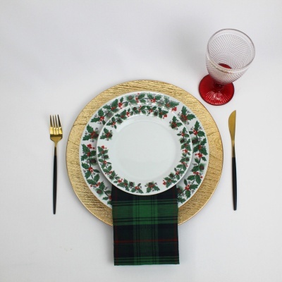 Conjunto de louças natalícias, talheres dourados e copo com base vermelha sobre fundo branco