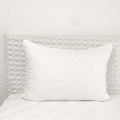 Travesseiro branco texturizado sobre cama e cabeceira acolchoada brancas