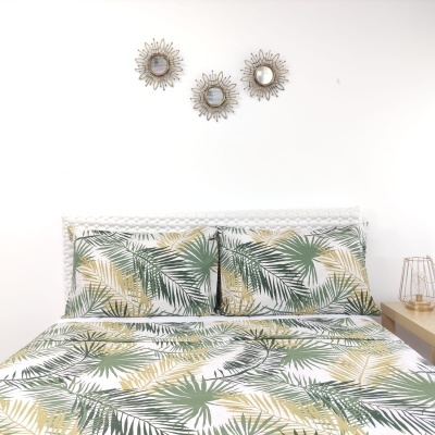 Conjunto de roupa de cama com padrão de folhas verdes e amarelas sobre fundo branco em quarto minimalista