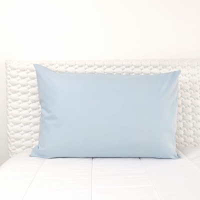 Travesseiro azul claro em cama branca com cabeceira acolchoada texturada