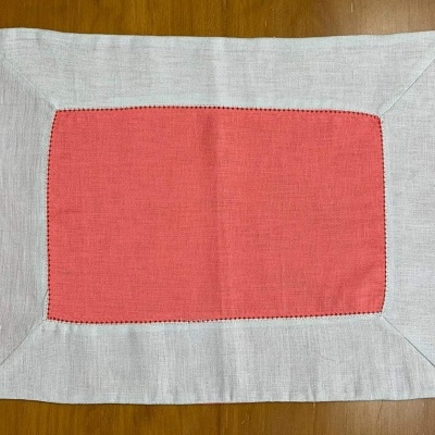 Toalha de mesa retangular coral com borda cinza claro sobre mesa de madeira