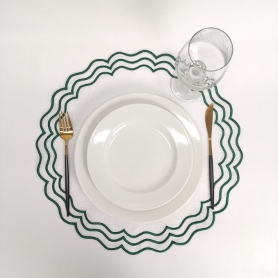 Conjunto de jantar com pratos brancos, talheres dourados e pretos, copo de vidro e toalha com borda verde ondulada