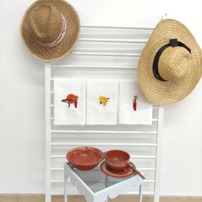 Toalhas brancas bordadas, chapéus de palha e utensílios de barro vermelho sobre mesa