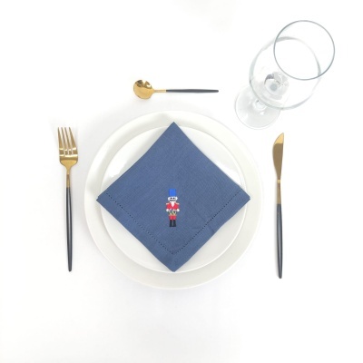 Conjunto de jantar com prato branco, guardanapo azul bordado, talheres dourados e pretos, e copo de vidro