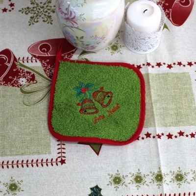 Pano de cozinha verde com bordado natalício sobre toalha festiva, ao lado de vela branca decorativa e jarra com flores.