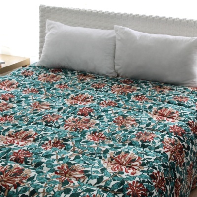 Colcha floral vermelha, verde e branca em cama branca com almofadas, mesa e janela