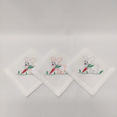 Três guardanapos brancos bordados com coelhos e cenouras