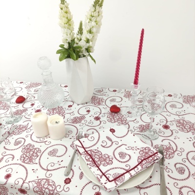 Mesa posta com toalha branca e vermelho, castiçal com vela vermelha, jarra e vaso com flores brancas