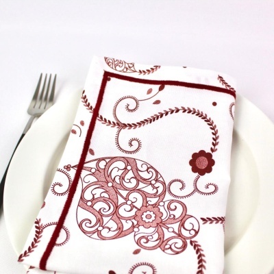 Guardanapo branco com padrão vermelho sobre prato branco e garfo ao lado