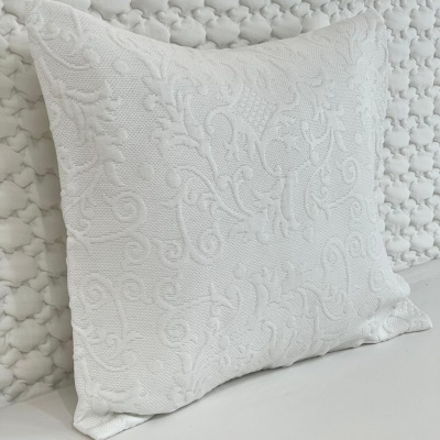 Almofada branca com padrão floral em relevo sobre tecido acolchoado branco