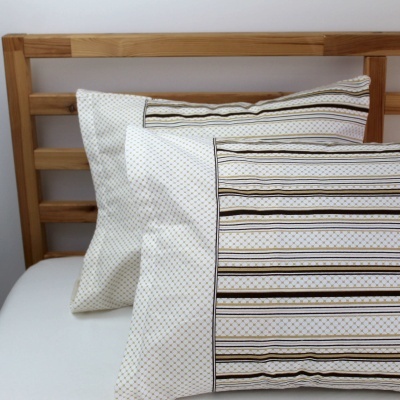 Duas fronhas decorativas com padrões geométricos e riscas em cama com cabeceira de madeira clara