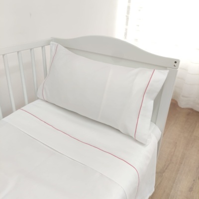 Jogo de cama infantil branco com bordos cor-de-rosa numa cama de grades branca