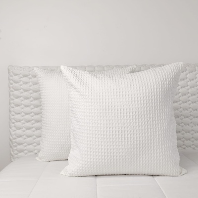 Duas almofadas brancas texturizadas sobre cama branca com cabeceira acolchoada branca